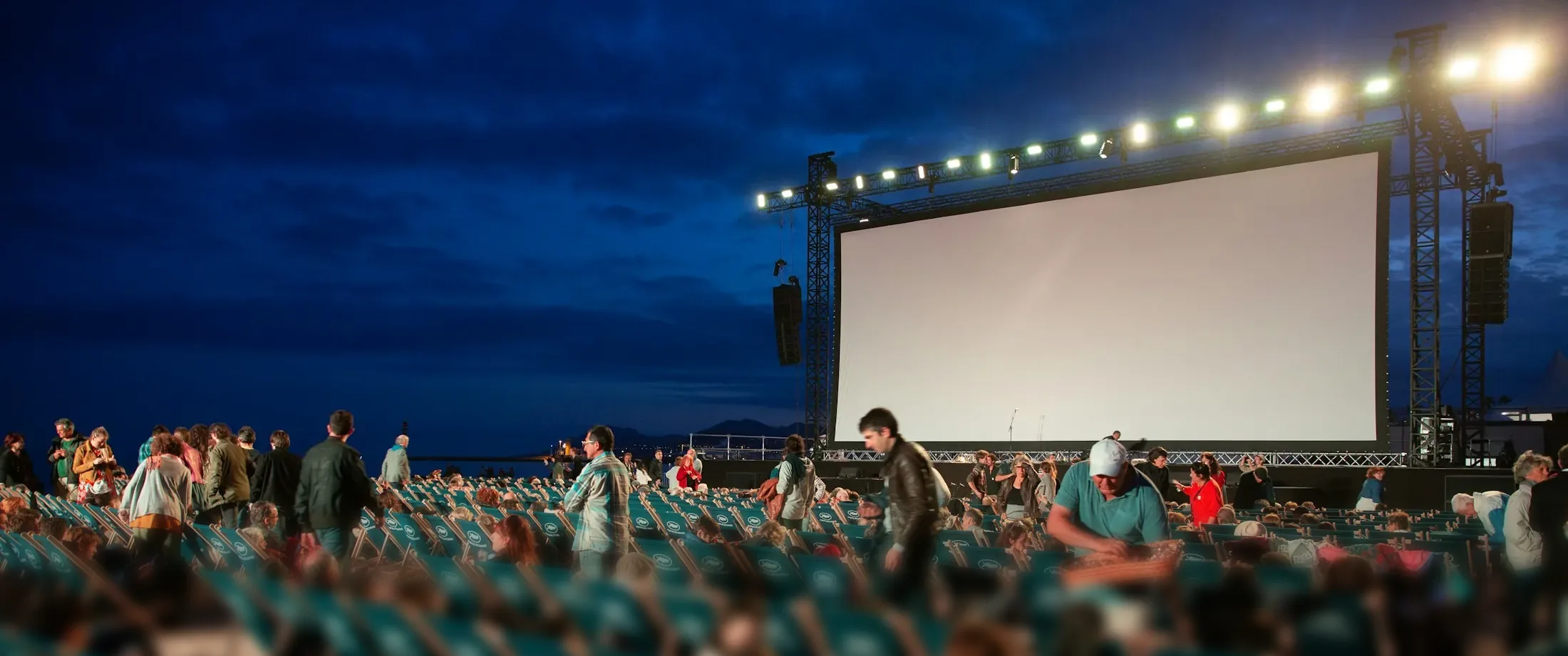 Grosse, noch leere Leinwand unter tiefblauem Abendhimmel, darüber eine Reihe Scheinwerfer. Davor Liegestühle und Publikum, das seine Plätze sucht.